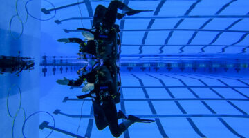A student wearing a wetsuit and SCUBA equipment is mirrored above and below the water's surface as they learn to SCUBA dive