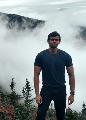 SuriyaPrakaash LakshmiBalasubramaniam standing on an overlook with a misty forest in the background.