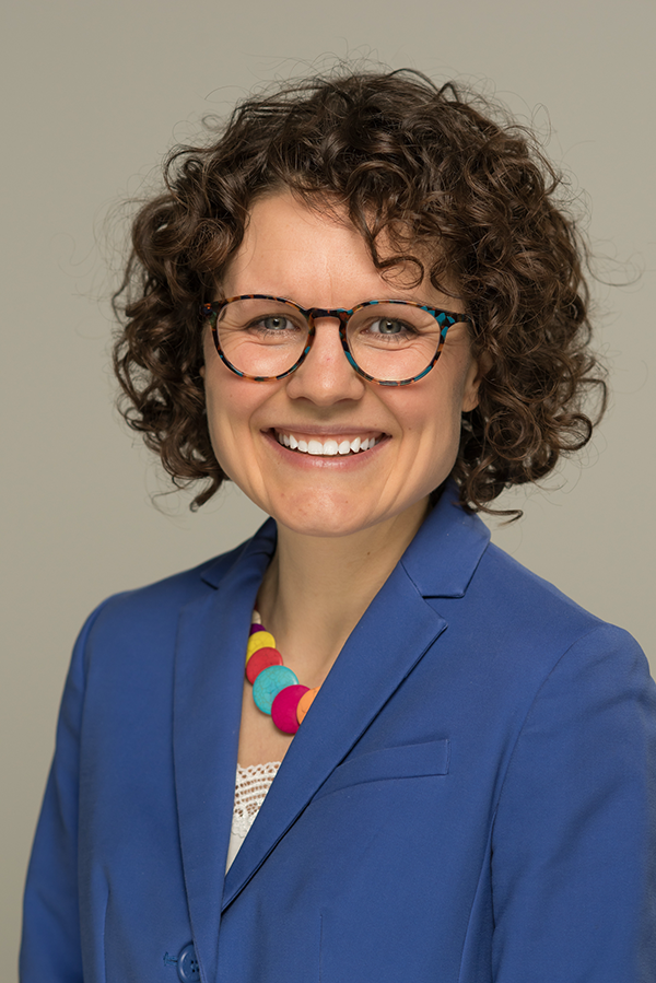 A portrait of Associate Dean Strout. She wears a blue blazer and has curly brown hair. She wears glasses and is smiling at the camera.