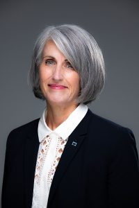 Portrait of Dean Diane Rowland. She has chin-length grey hair and is smiling at the camera. She is wearing a white shirt and black blazer.