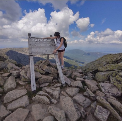 Anderson poses with a wood sign at the summit of Mount Katahdin.