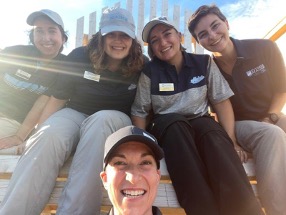 Five members of the survey research team sit on a bench and smile for a photo. They are wearing nametags and UMaine garb.