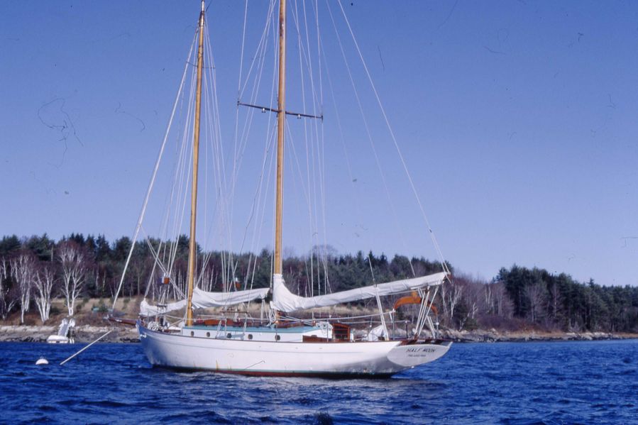 white schooner with sails down sits at anchor in front of the Darling Marine Center