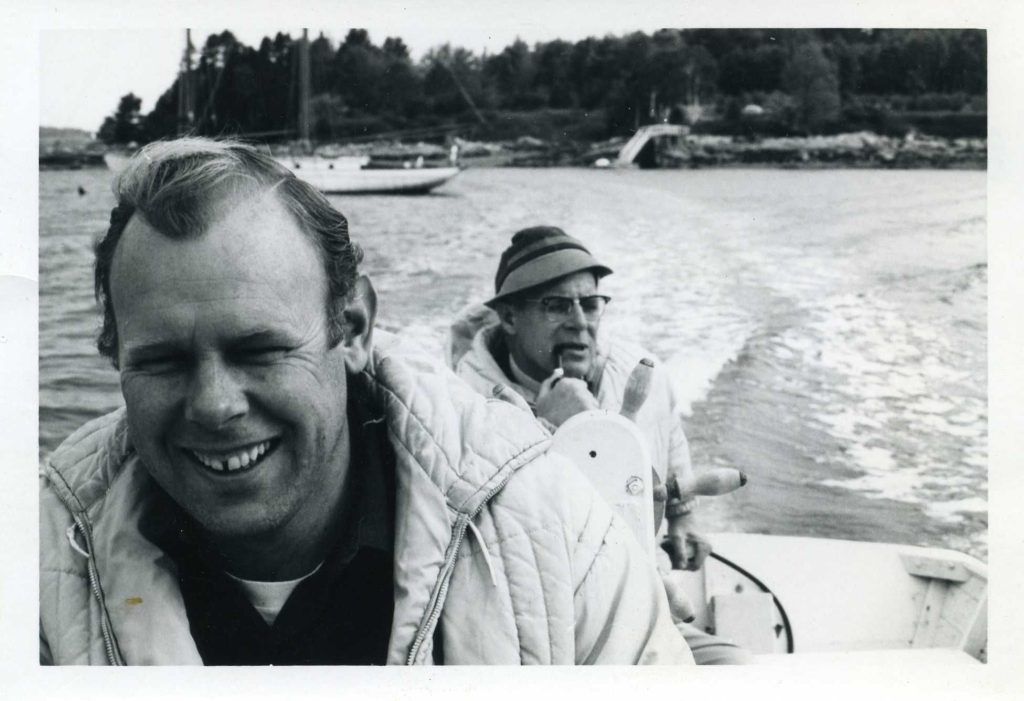 two men sit in boat while one smokes a pipe